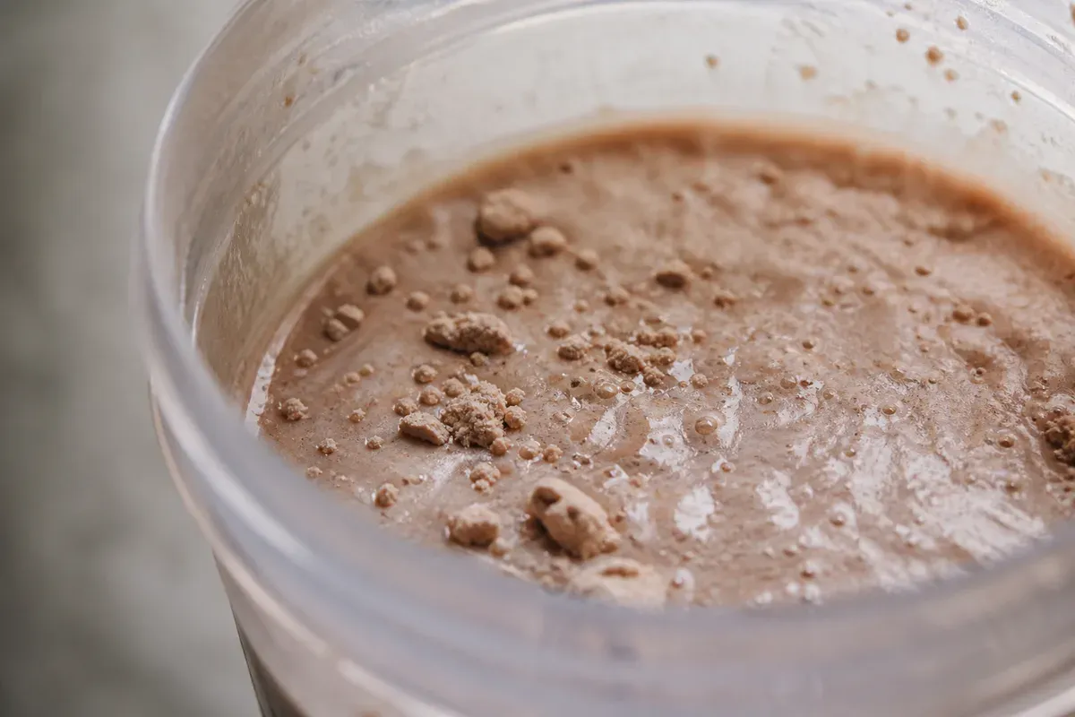 Shake de whey mal dissous dans un shaker transparent, avec des grumeaux de poudre non mélangée en surface